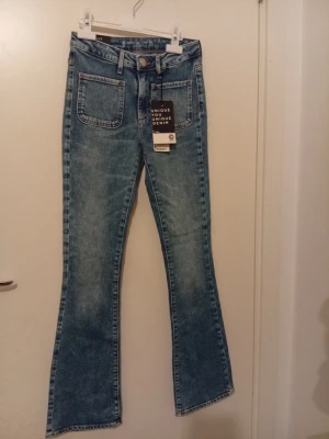 Blå 70's flare jeans från Pssst! Denim - Säljer ett par blå 70's flare jeans från Pssst! Denim i storlek 25. Jeansen har låg midja, med bootcut och två fickor fram. Materialet är klassisk jeans med snygg tvättad look och orangea sömmar. Perfekt för dig som gillar retrostil. Är helt ny och inte använd och har pris lapen kvar och så.