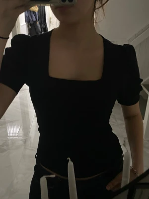Svart topp med puffärm och fyrkantig hals - Säljer en svart topp med korta puffärmar och snygg fyrkantig halsringning. Modellen är figurnära och har en stilren, enkel design som är lätt att matcha. Materialet känns mjukt och stretchigt, perfekt för dig som gillar en clean look med lite edge. OBS säljer exakt likadan i VITT också!
