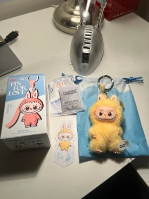 Gul pälsväst från Pop Mart The Monsters - Supergullig väst i fluffig gul pälsimitation från Pop Mart The Monsters. Västen har kaninöron och är designad som en del av en nyckelringsfigur. Perfekt för dig som gillar unika accessoarer och vill sticka ut med något lekfullt och färgglatt.