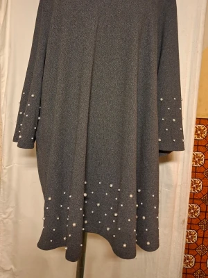 Grå långärmad tröja med pärlor Zizzi - Snygg grå långärmad tröja från Zizzi i storlek XL. Tröjan har pärldetaljer på ärmarna och nedtill, vilket ger en extra touch. Modellen är loose fit och har en mjuk, stickad känsla. Perfekt för dig som gillar stilrena plagg med lite extra.