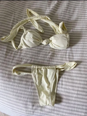 Krämvit bikini - Bikini krämvit färg med knyt både på toppen och trosorna. Toppen har en snygg knut framtill och axelbanden kan justeras med knyt. 