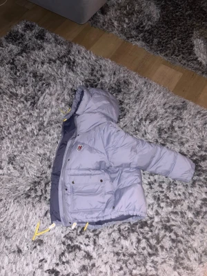 Ljusgrå Fjällräven Expedition dunjacka - Hjälper min flickvän sälja sin Fjällräven Expedition dunjacka. Jackan har långa ärmar, två stora fickor med knappar framtill och dragkedja. Insidan är mörkblå och jackan är quiltad för extra värme. Perfekt för kalla vinterdagar. Den är L men passar på henne som en M