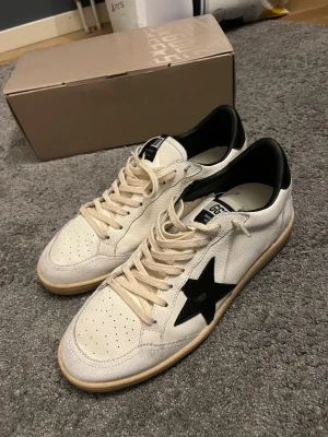 GCDS vita sneakers med svart stjärna - Säljer ett par vita sneakers från GCDS med svart stjärna på sidan och svart häl. Skorna har snörning, perforerad tå och texten 'SNEAKERS' broderad på baksidan. Tillverkade i skinn med platt sula och rund tå. Snygga detaljer och box medföljer.