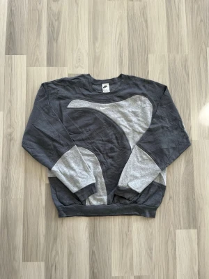 Vintage Nike Sweatshirt  - Säljer en grå och ljusgrå limited sweatshirt från Nike med ett stort, böljande mönster framtill och på ärmarna. Tröjan har rund hals och långa ärmar, samt en liten broderad Nike-logga på bröstet. Perfekt för dig som gillar sportig och avslappnad stil. Tröjan är i oanvänt skick! 