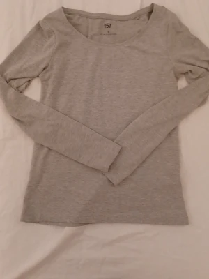 Grå långärmad topp  - Säljer en enkel och stilren grå långärmad topp från lager 157 i storlek S. Toppen har rund halsringning och är gjord av mjuk bomullsmix med lite stretch för skön passform. Perfekt att matcha med jeans eller kjol.