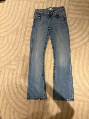 Blå bootcut jeans med fem fickor - Säljer ett par ljusblå jeans med klassisk bootcut passform och fem fickor. Jeansen har normal midja och är tillverkade i mjukt denimtyg. Perfekt för dig som gillar en avslappnad stil med lite utsvängda ben.