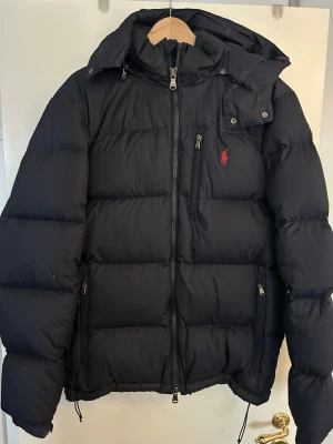 Marinblå Polo Ralph Lauren vinterjacka L  - Polo Ralph Lauren Marinblå pufferjacka Water-Repellent Down Jacket i storlek L inköpt på Boozt oktober 2023 och användes i en säsong. Nypris då var 4895:- På ena ärmen finns ett litet hål som kan täckas över med lagninglapp. 
