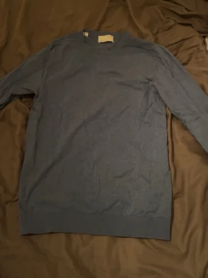 Blå stickad tröja från Selected Homme storlek S - En stilren blå stickad tröja från Selected Homme. Tröjan har rund halsringning och långa ärmar, perfekt för lager på lager under kyligare dagar. Enkel och clean design som funkar till det mesta.