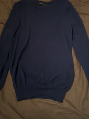 Marinblå stickad tröja J.Lindeberg storlek S - Snygg marinblå stickad tröja från J.Lindeberg i storlek S. Tröjan har rund hals och långa ärmar, perfekt för dig som gillar stilrena och klassiska plagg. Materialet är mjukt och skönt, passar bra till både jeans och chinos.