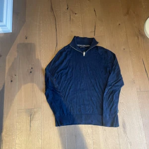 Blå half zip tröja från Jack & Jones - Snygg mörkblå långärmad tröja från Jack & Jones med half zip och hög krage. Tröjan är i mjuk bomull och har ribbade muddar vid ärmslut och nederkant. Perfekt för dig som gillar enkel och stilren design.