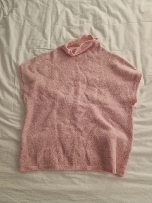 Rosa stickad polotröja från Lindex - Mysig rosa stickad polotröja från Lindex i storlek M. Tröjan har en lös passform och är ärmlös, vilket gör den perfekt att bära över en långärmad topp eller som den är. Den har en mjuk och fluffig känsla med ribbad kant nedtill och vid halsen.