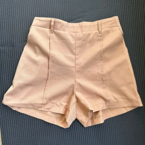 Beige höga shorts med resår i S. - •Mycket snygga beige shorts med hög midja och resår baktill. •De har en stilren look med pressveck framtill & plats för skärp. •Enkel och clean stil. •Oanvända, endast tvättade. •Skärp ingår inte.