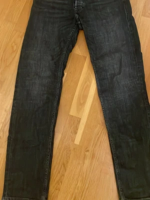 Svarta jeans Tapered Mike 31/32 - Svarta jeans från Tapered Mike i storlek 31/32. Jeansen har en snygg tvättad look och klassisk femficksdesign med raka ben och diskreta sömmar. Passformen är tapered vilket ger en modern siluett. Perfekta för dig som gillar stilrena och bekväma jeans.
