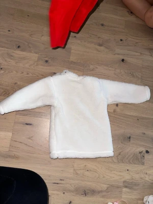 Vit fluffig långärmad tröja Vit tröja - Supermjuk och fluffig vit tröja med lång ärm, perfekt för kyliga dagar. Materialet är fleece som ger en mysig känsla och håller dig varm. Enkel design utan mönster eller detaljer, passar dig som gillar stilren och bekväm look.Vit, mjuk tröja med långa ärmar. 