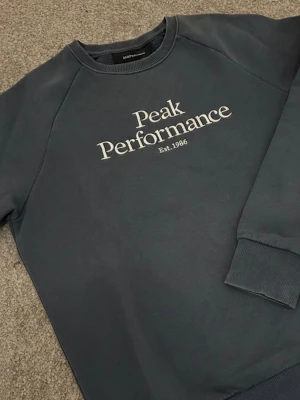 Mörkblå Peak Performance sweatshirt - Säljer en mörkblå sweatshirt från Peak Performance. Tröjan har rund hals, långa ärmar och ribbade muddar vid ärmslut och nederkant. Perfekt för dig som gillar en stilren look. Tröjans färg är minimalt förändrad på vissa ställen pga tvättning, helhetsintrycket är dock i princip oförändrat. (se bilderna). Tröjan har inga defekter. Nypris: 1000kr. Mitt pris: 199kr. Modellen är 183cm, 72kg men tröjan passar även mindre då den är lite för liten för mig. Hör av dig vid frågor. Pris kan diskuteras.