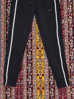 Hugo Boss byxer - Svarta mjukisbyxor från BOSS med vita ränder längs benen, snörning i midjan och dragkedja på fickorna. Byxorna har en slim passform och är tillverkade i mjukt bomullsmaterial. Perfekta för en chill och sportig look. Har använt de 2-3 gånger. Inga tecken på användning 