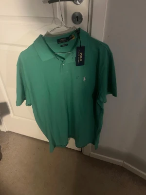Grön pikétröja Polo Ralph Lauren - Säljer en grön pikétröja från Polo Ralph Lauren i modellen Custom Slim Fit. Tröjan har klassisk krage, två knappar framtill och den ikoniska broderade loggan på bröstet. Tillverkad i bomull och perfekt för en clean och stilren look.skicka om mer information skicka om du vill ha bild på när man har på sig den 