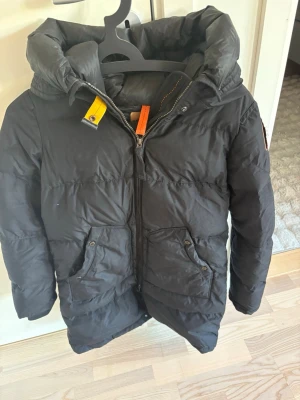 Svart Parajumpers dunjacka med huva - Svart dunjacka från Parajumpers med stor huva. Säljs på grund av att jag har slutat använda den och den är använd sammanlagt 6 månader på 3 år. Inga hål eller något liknande på jackan. Pris kan diskuteras. Jackan är äkta och kvitto finns också
