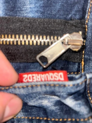 Dsquared2 blå skinny jeans med dragkedja - Säljer ett par blå Dsquared2 jeans med skinny passform och coola slitningar samt hål på framsidan. Jeansen har en stor dragkedja framtill och tydliga vita tvättade detaljer. Klassisk femficksmodell med röd etikett vid gylfen