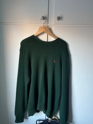Mörkgrön stickad tröja Polo Ralph Lauren - Säljer en mörkgrön stickad tröja från Polo Ralph Lauren i storlek L. Tröjan har en klassisk rund hals, långa ärmar och en liten orange broderad logga på bröstet.  Kontakta mig vid flera frågor😃