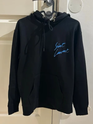 Saint Laurent Hoodie med blå text - Helt ny Saint Laurent hoodie med blå text i storlek M men passar även S. Fraktar den inom 24 timmar efter köp🚛📦