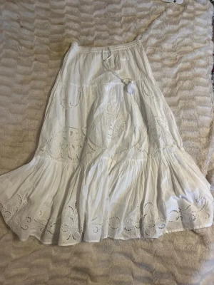 Långkok vit  - Lyxig och Supersnygg vit långkjol med broderade detaljer och snörning i midjan. Kjolen har ett luftigt fall och fina hålbroderier som ger en bohemisk vibe. Perfekt för varma dagar och ger en chill och romantisk look. Nypris 700kr. 