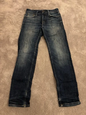 Jack and Jones Tapered/Mike jeans - Säljer ett par Jack and Jones Tapered/Mike jeans i mörkblå tvätt med snygga slitningar. Klassisk femficksmodell med normal passform och raka ben. Jeansen har en modern look som funkar till det mesta.