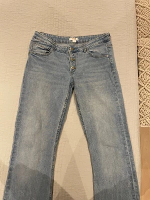 Bootcut jeans från Gina Tricot ljusblå - Snygga ljusblå bootcut jeans från Gina Tricot med klassisk femficksdesign och knappgylf. Jeansen har en rak passform över låren och lätt utsvängda ben. Tillverkade i mjukt denimtyg som ger en skön känsla och cool look.