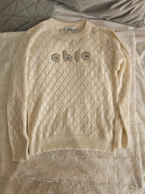 Jättegullig beige stickad tröja med pärldetaljer - Jag säljer denna jättegulliga beigea stickade tröjan från Fullamoda med pärlbroderade bokstäver 'chic' framtill. Rund hals och långa ärmar. Aldrig använd och därför i mycket bra skick. Jättefin att matcha till exempel jeans, linnebyxor eller kostymbyxor. 💓💓