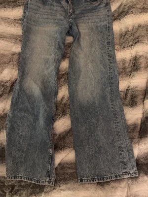 Blå straight jeans från Divided, stl 42 - Säljer ett par blå jeans från Divided i storlek 42. De har en cool tvättad look och breda ben, med knapp och dragkedja framtill. Perfekta för dig som gillar loose fit. 💗