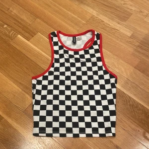Rutig linnetopp från H&M Divided XS - Säljer en rutig linnetopp från H&M Divided i storlek XS. Toppen har svartvitt schackrutigt mönster och röda kanter runt hals och ärmhål. 