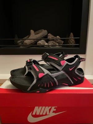Nike ACG sandaler svart/rosa - Nike ACG sandaler i svart och grått med rosa detaljer. Justerbara remmar med kardborre och robust sula med grepp. 