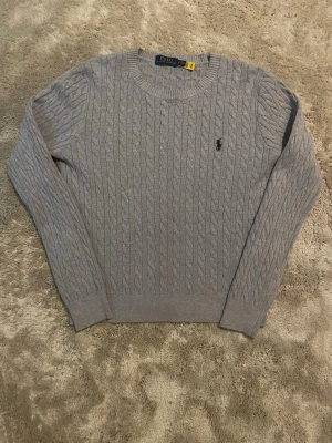 Ljusgrå kabelstickad tröja Polo Ralph Lauren - Säljer denna raplh lauren i 100 % bomulls material. Använd max 1-2 gånger då jag fick den i julklapp och den var för liten. Jag är 178 cm lång och den borde passa dig som är max 173 cm lång. Skickas endast med PostNord. Om annat fraktsätt väljs av Plick, avbryts köpet.