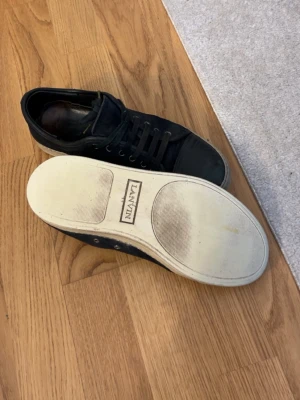 Svarta sneakers från Lanvin i mocka helst byta  - Säljer ett par svarta sneakers från Lanvin med ovandel i mocka och tåparti i skinn. Skorna har snörning, rund tå och vit platt sula med Lanvin-logga undertill. Klassisk och stilren modell som passar till det mesta.
