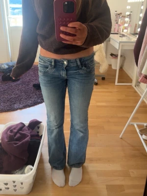 Blå bootcut jeans Gina Tricot 164 - Säljer ett par ljusblå bootcut jeans från Gina Tricot i storlek 164. Jeansen har låg midja, klassiska fem fickor och snygg tvättad look. Tillverkade i jeansmaterial med dragkedja och knapp framtill.