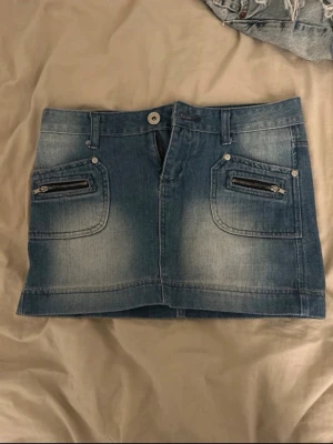 Blå jeanskjol med dragkedjor - Säljer en snygg blå jeanskjol i kort modell med slitna detaljer och två coola dragkedjor framtill. I storlek 164 men passar Xs!!! 