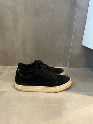 Svarta mockasneakers från Vagabond - Säljer ett par stilrena svarta sneakers från Vagabond i mjuk mocka. Skorna har svarta snören och en kontrasterande vit sula som ger en clean look. Perfekta till jeans eller mjukiskläder  för en avslappnad vibe. Nypris 1300kr säljs för 299kr. Innan de postas kan jag använda mocka borste. 
