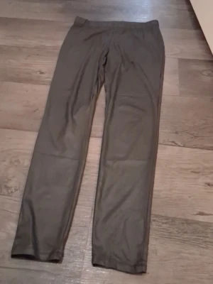 Svarta fejkskinnleggings storlek L - Säljer ett par svarta mjukisbyxor från C i storlek L. Byxorna har elastisk midja och är tillverkade i ett mjukt och stretchigt material som känns skönt mot huden. Perfekta för chill dagar eller när du vill ha det bekvämt.