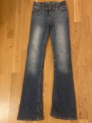 Blå bootcut jeans med slitningar - Snygga blå jeans med bootcut-snitt och lätt slitna detaljer på framsidan och baksidan. Klassisk femficksmodell med knapp och dragkedja i midjan. Jeansen har en cool tvättad look och är tillverkade i jeansmaterial som ger en skön känsla.