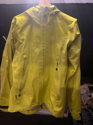 Gul Haglöfs Gore-Tex skaljacka - Gul skaljacka från Haglöfs i storlek S. Jackan är tillverkad i slitstark polyester med Gore-Tex Active-membran, två fickor med dragkedja och justerbara ärmslut och huva. En lättviktad vatten och vindtät jacka som jag själv har använt i skidbacken. Väldigt fint skick