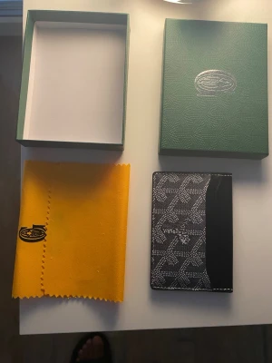 Svart plånbok med mönster - Säljer en stilren svart plånbok med deras ikoniska grafiska mönster. Plånboken har flera kortfack och är tillverkad i skinn med detaljer i canvas. Perfekt för dig som vill ha något lyxigt och klassiskt i fickan.