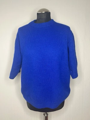 Kornblå stickad tröja från H&M - En kornblå stickad tröja från H&M i storlek S. Tröjan har rund halsringning och trekvartsärm, vilket ger en avslappnad men ändå stilren look. Perfekt att bära över ett linne eller t-shirt för extra lager.