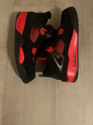 Nike Air Jordan 4 svart/röd sneakers/ red thunder (utan lappar och låda)  - Säljer ett par Nike Air Jordan 4 sneakers i svart och rött med meshdetaljer och klassisk Jumpman-logga på tungan och sulan. Skorna har snörning, platt sula och coola plastdetaljer vid snörningen. Ovandelen är i syntet och mocka för en schysst look.