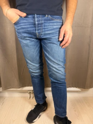 Blå skinny jeans från American Eagle - Säljer ett par blå skinny jeans från American Eagle. Jeansen har klassisk femficksdesign, normalhög midja och snygga slitningar framtill. Materialet är mjukt jeans-tyg i bomull och passformen är tight hela vägen ner.