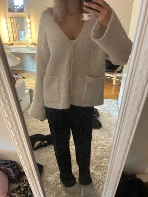 Beige fluffig kofta från Pieces - Mysig beige kofta från Pieces i fluffigt stickat material. Koftan har v-ringning, två stora framfickor och stängs med två knappar framtill. 