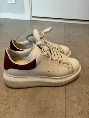 Sneakers från Alexander McQueen - Säljer ett par vita Alexander McQueen skor med vinrött där bak. Skorna är köpta från Vestiaire i nyskick och är använda mycket sparsamt under en höst och vår. De har en slitning i hälen på ena skon men är inget som känns. Storlek 36, köptes för 3000kr men säljer för 1500❤️