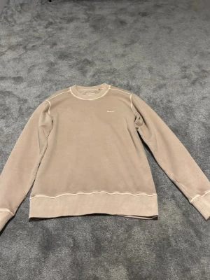 Beige sweatshirt från GANT - Säljer en stilren beige sweatshirt från GANT i storlek XS. Tröjan har rund halsringning, ribbade muddar och diskret GANT-logga broderad på bröstet. Con 6/10 därav det låga priset