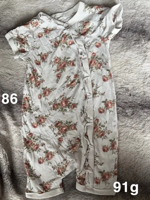 Blommig vit kortärmad pyjamas  - Supersöt vit kortärmad pyjamas med blommigt mönster i rosa och grönt. perfekt för varma dagar. Tryckknappar framtill gör den enkel att ta på och av. Perfekt för en gullig och bekväm stil.🌸 Fint använt skick. Storlek 86