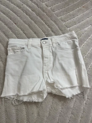 Vita jeansshorts från GANT - Säljer ett par vita jeansshorts från GANT med råa, fransiga kanter och klassisk femficksdesign. Shortsen har hög midja och är gjorda i mjuk bomull med knapp och dragkedja framtill. Perfekta för varma dagar och chill stil. Pris går att diskutera.