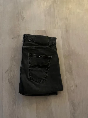 Svarta jeans från Nudie Jeans - Säljer ett par svarta jeans från Nudie Jeans. Jeansen har rak passform och är tillverkade i slitstarkt denimtyg. Perfekt för dig som gillar stilrena och tidlösa jeans. Jeansen är använda få gånger! Knappen på byxorna är trasig men går enkelt att laga.